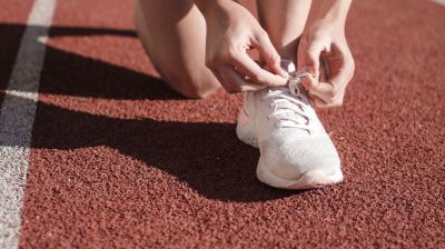Füße eines Sprinters oder einer Sprinterin auf der Laufbahn beim Zubinden der Schnürsenkel des einen Laufschuhs